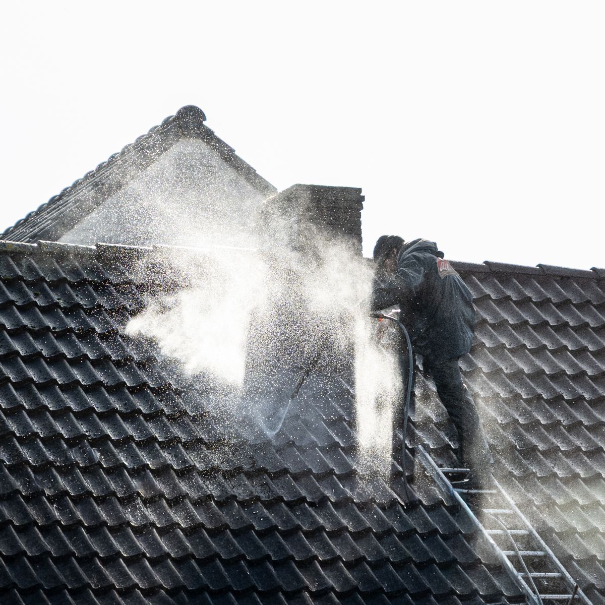Worker washing a roof before treatment
